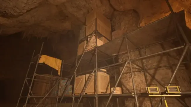 Scaffolding, stacked wooden crates, and portable lights in an excavation cavern