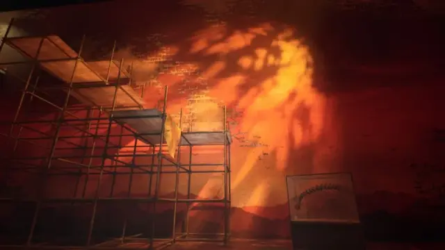 Scaffolding and a yellow-cloth ledge beside the orange exhibit wall